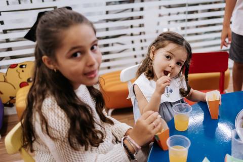 Foto de close de crianças sorrindo e comendo na mesa principal.'