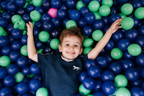 Foto de uma criança deitado de braços abertos na piscina de bolinhas.'