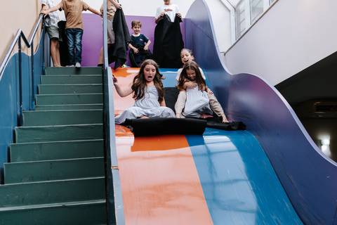 Foto aproximada de crianças se divertindo no escorregador colorido.'