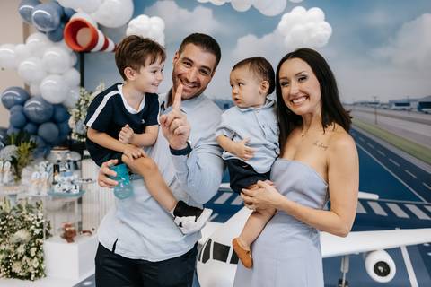 Foto dos pais com aniversariante e convidado na frente da mesa principal. '
