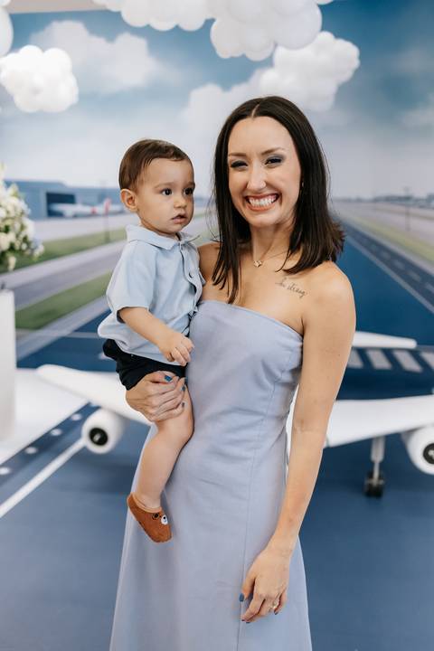 Foto da mãe segurando o aniversariante no colo em frente ao painel.'