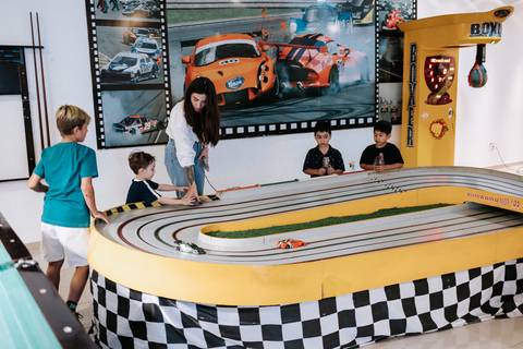 Foto da pista de autorama com crianças e adultos interagindo.'