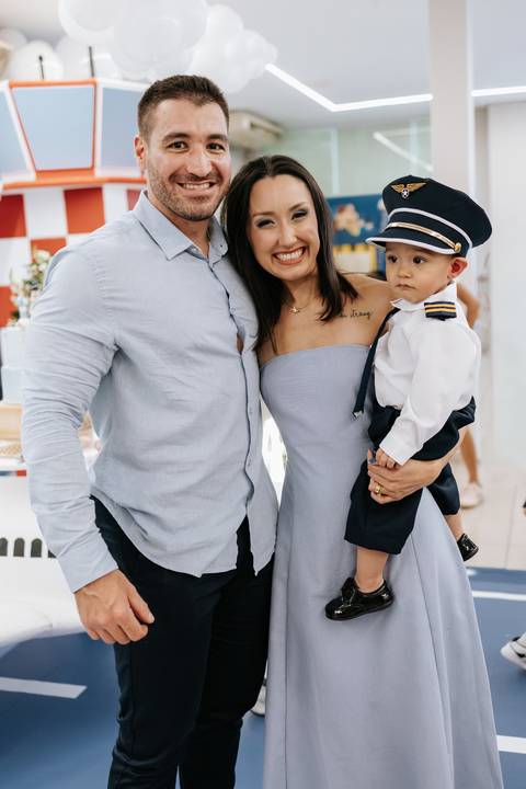 Foto dos pais sorridentes com o pequeno piloto pronto para o voo.'