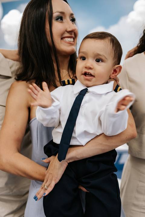 Foto aproximada do aniversariante batendo palmas no colo da mãe.'