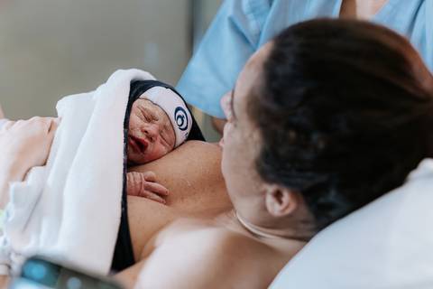 Foto de close do bebê no contato pele a pele com a mãe.'