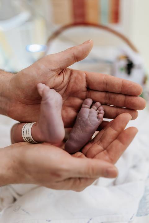 Foto em detalhe dos pezinhos do recém-nascido nas mãos do pai.'