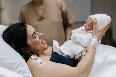 Foto da mãe deitada na maca segurando o bebê Guilherme no colo.'