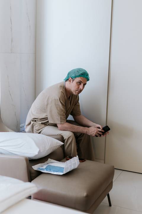 Foto do pai sentado e paramentado aguardando no quarto hospitalar.'