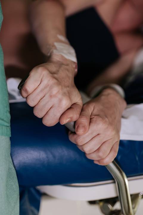 Foto em detalhe das mãos da gestante segurando o apoio da maca.'