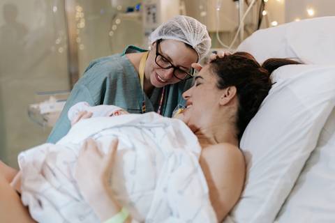 Foto da mãe sorrindo para a equipe médica com o bebê.'