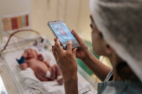 Foto da irmã fotografando o bebê no berço aquecido.'