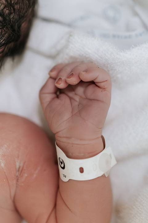 Foto em detalhe da mãozinha do recém-nascido com a pulseira de identificação.'