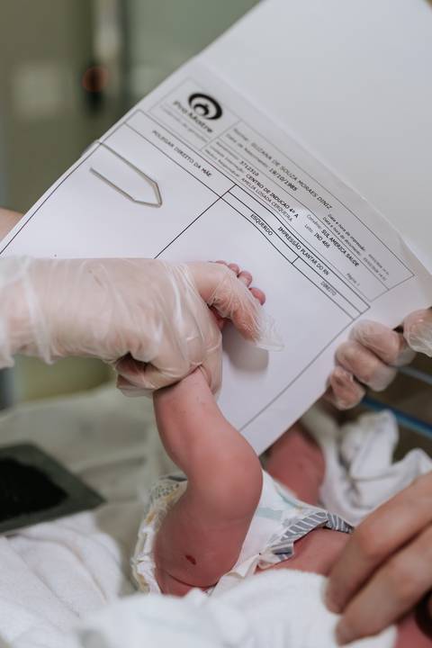 Foto da equipe médica realizando o carimbo do pezinho no prontuário.'