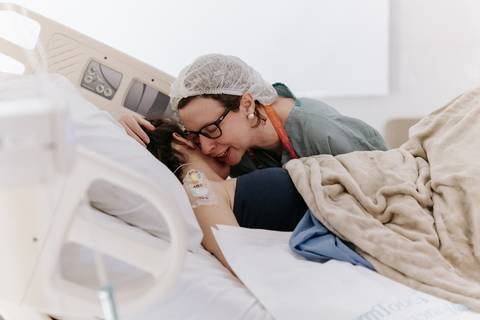 Foto da mãe recebendo carinho e suporte da equipe no pós-parto.'