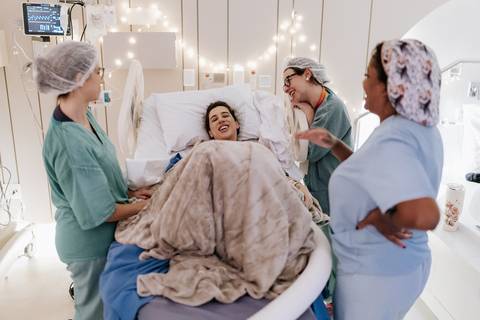 Foto da mãe descansando na maca cercada pela equipe de parto.'