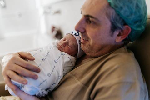 Foto do pai segurando o Guilherme embrulhado em manta.'