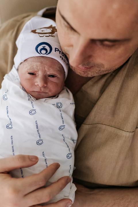 Foto aproximada do pai abraçado ao filho recém-nascido.'