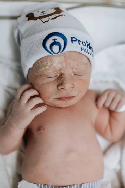 Foto em macro das mãos do bebê próximas ao rosto.'