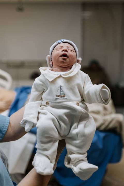 Foto aproximada do bebê com seu macacão de saída de maternidade.'