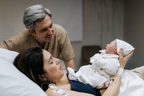 Foto do casal observando o filho recém-nascido na maca hospitalar.'