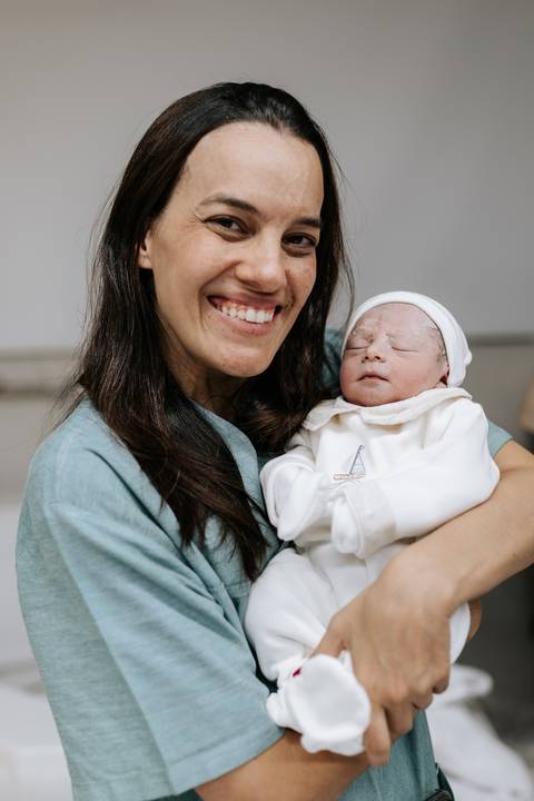 Foto da irmã sorrindo e segurando o bebê no colo.'