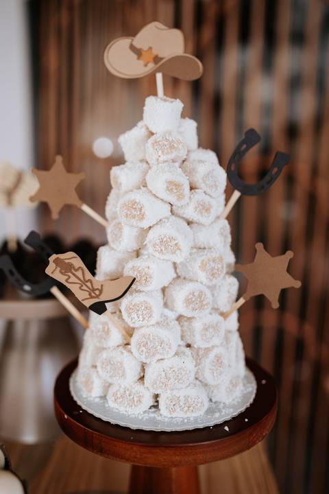 Foto em detalhe de torre de marshmallows decorada com itens de fazenda.'