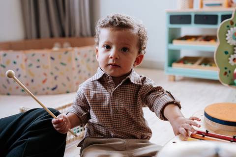 Foto do aniversariante sentado no chão brincando com baquetas.'