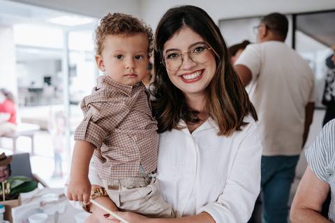 Foto da mãe sorridente segurando o aniversariante no colo.'