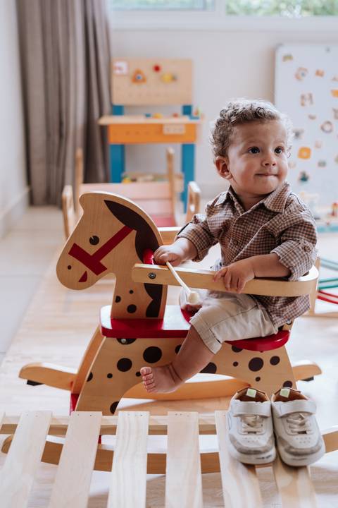 Foto do aniversariante montado em um cavalo de balanço de madeira.'