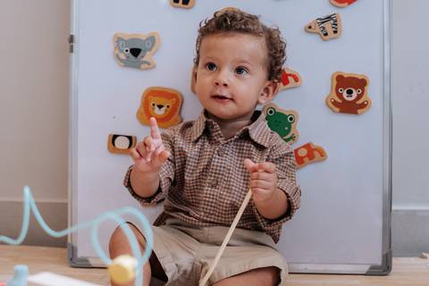 Foto do Thomas sorrindo e apontando para o brinquedo no chão.'
