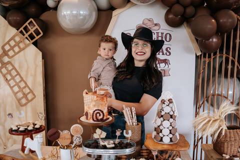 Foto da mãe segurando o aniversariante na mesa do bolo temática.'