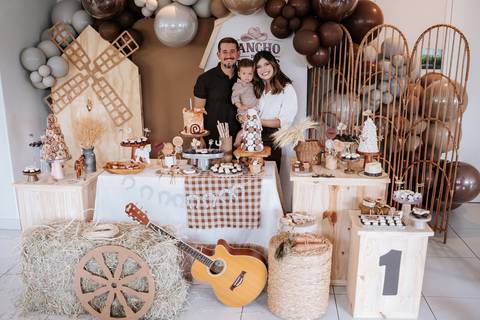 Foto panorâmica da mesa de doces completa com decoração rústica e balões.'