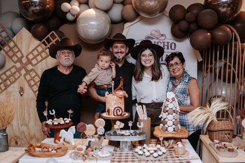 Foto da família reunida (pais e avós) atrás da mesa principal decorada.'