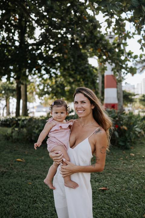 Foto da mãe e filha sorridentes posando para a câmera ao ar livre.'
