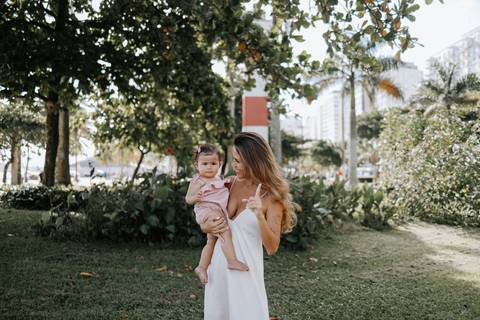 Foto da mãe caminhando no jardim enquanto segura a pequena no colo.'