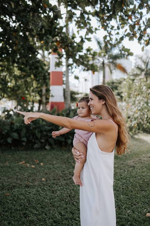 Foto da mãe apontando para o horizonte enquanto segura a filha no colo.'