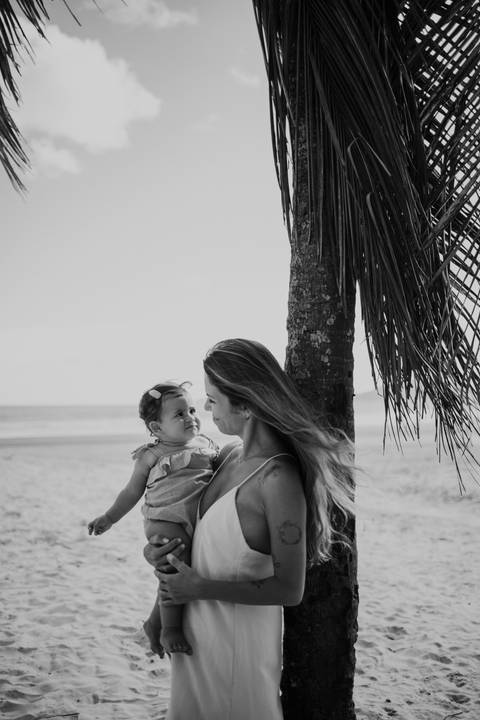 Foto em preto e branco da mãe e filha trocando olhares de afeto na praia.'
