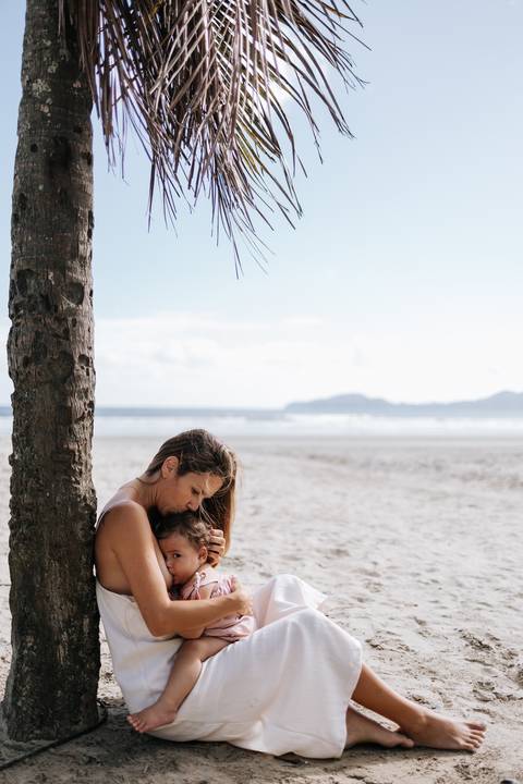 Foto aproximada da mãe beijando a cabeça da filha na beira-mar.'