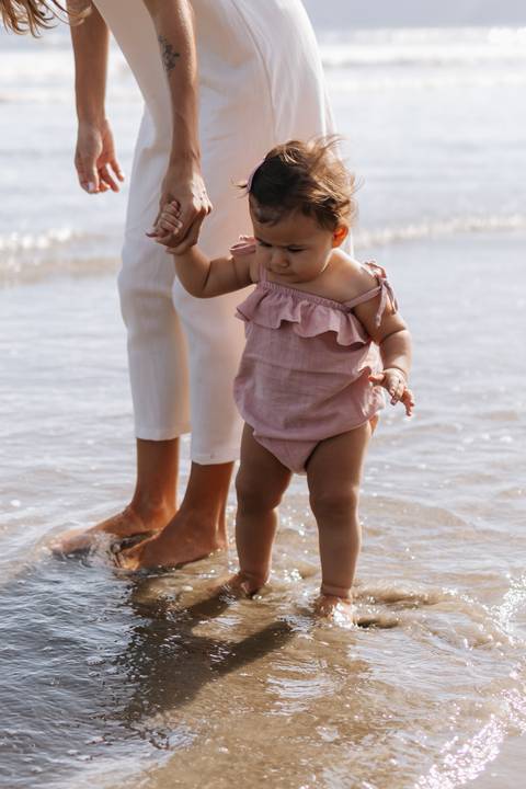 Foto em detalhe dos pés da mãe e da filha na areia molhada.'