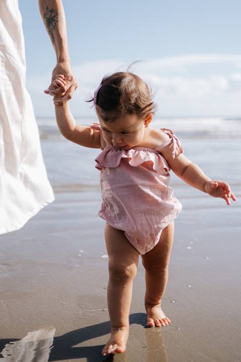 Foto aproximada da bebê explorando a areia com seu romper rosa.'