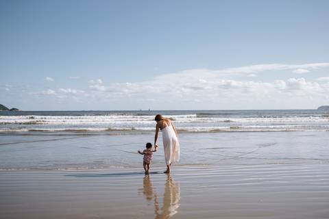 Foto panorâmica da mãe e filha sozinhas na imensidão da praia.'
