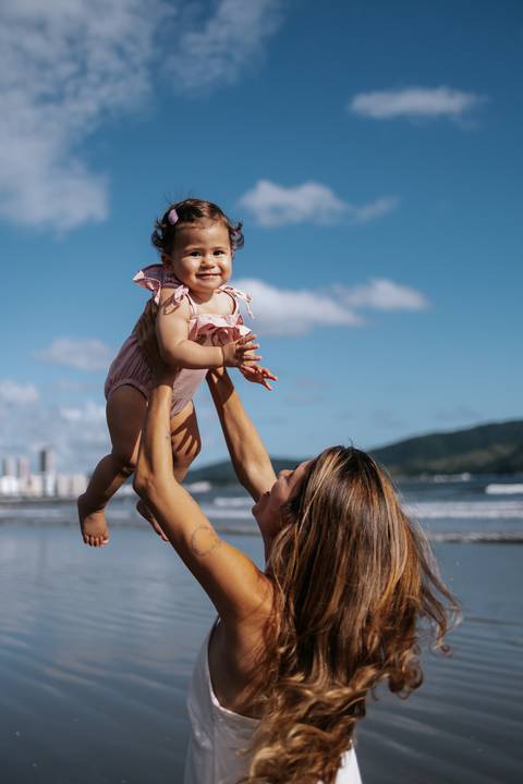 Foto da mãe erguendo a filha para o alto em momento de celebração.'