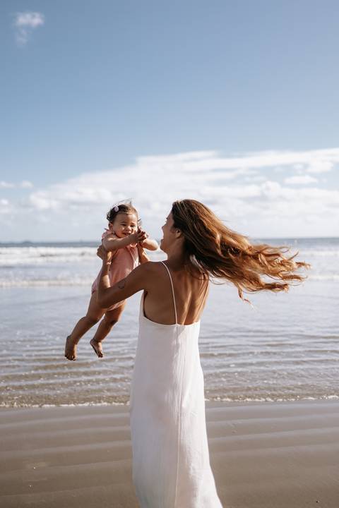 Foto da mãe girando com a filha no colo em momento de diversão.'