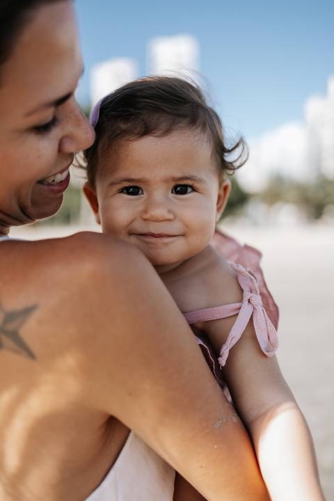 Foto aproximada do rosto da bebê sorrindo no colo materno.'