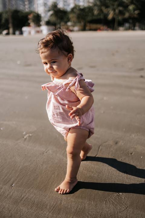 Foto em detalhe da bebê caminhando sozinha pela areia firme.'