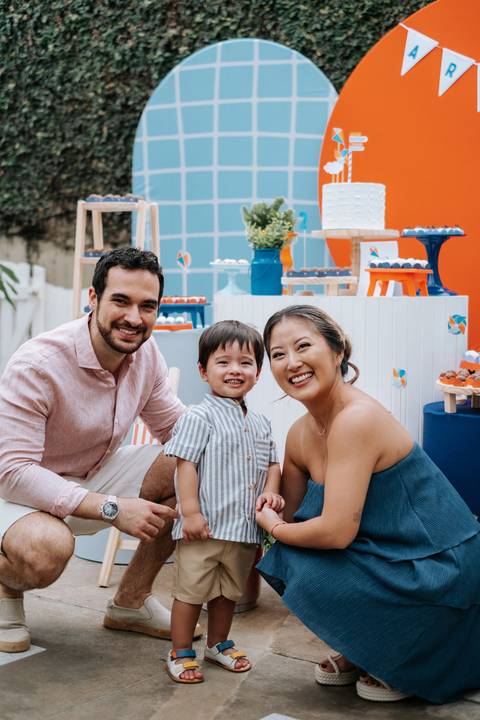 Foto do casal e o filho sorrindo sentados próximos à mesa principal.'