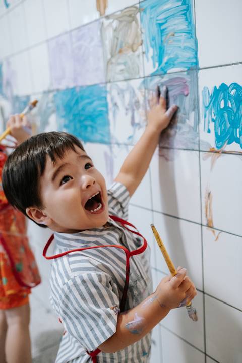 Foto do Arthur se divertindo e pintando em um azulejo.'
