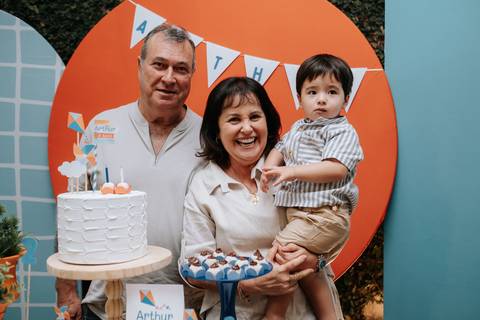 Foto do aniversariante com os avós na mesa do bolo decorada.'