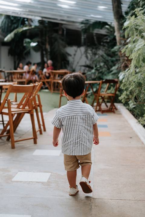 Foto do aniversariante de costas caminhando pelo salão de festas.'