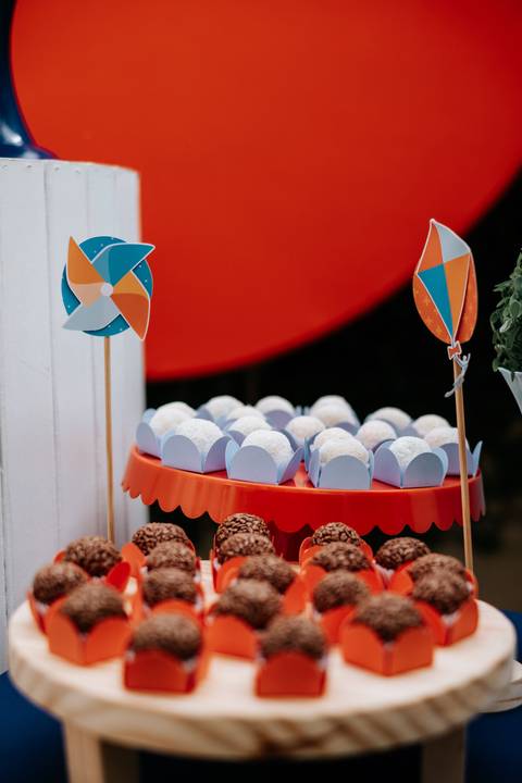 Foto em detalhe de docinhos de festa com enfeites de catavento ao fundo.'